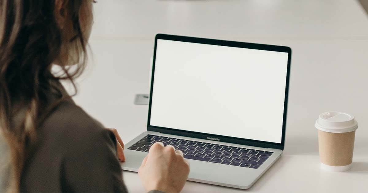 An over the shoulder photo of a woman using a laptop on a clean conference room table