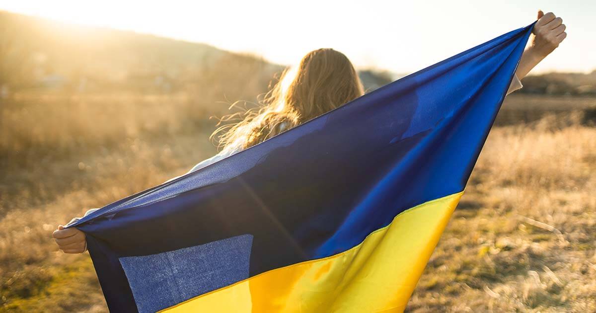 A woman holding a Ukraine flag in a grassy golden field